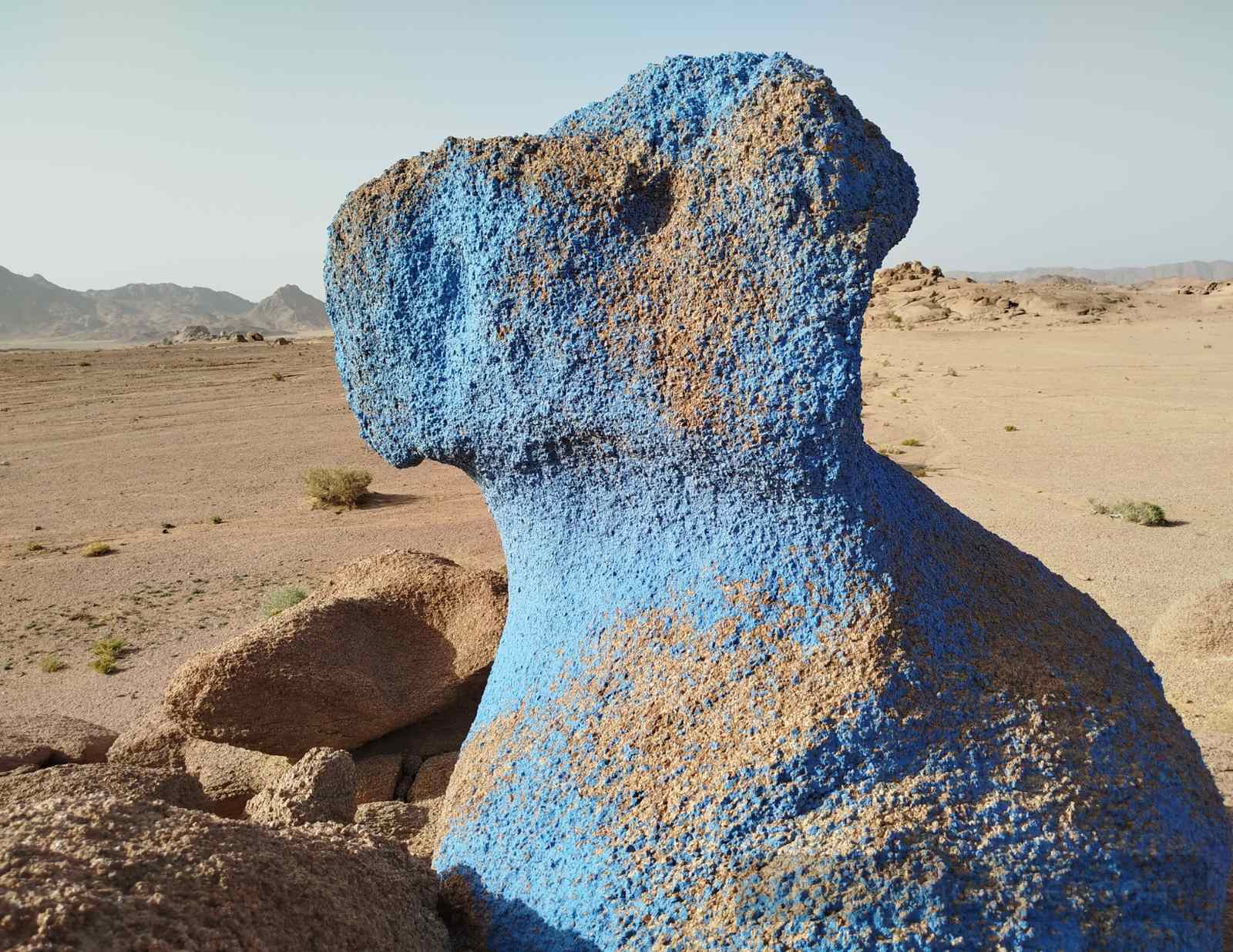 Blue-painted rock formation in the Blue Desert of South Sinai, created by artist Jean Verame, standing on a sandy plain with distant mountains.