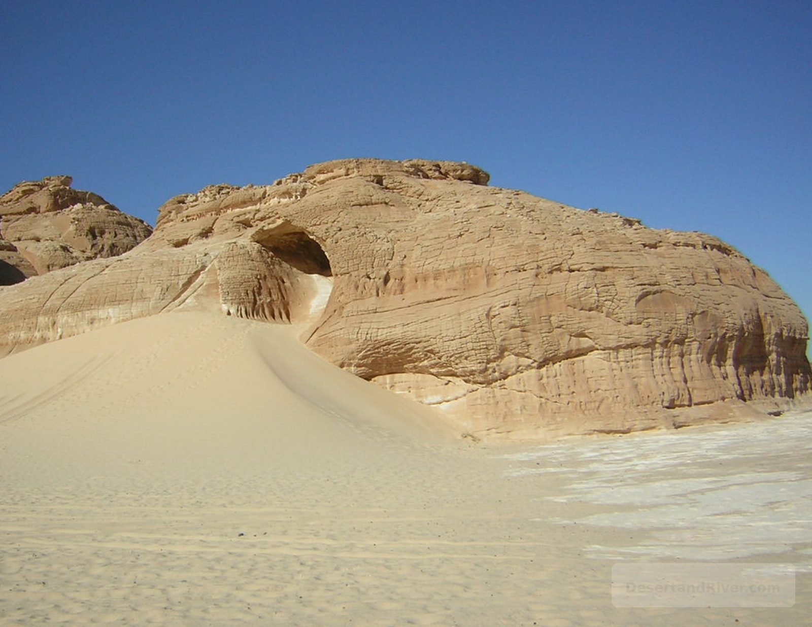 Gebl Makhroom (Dragon Head Mountain) in southern Sinai, a wind-eroded sandstone formation with a hollow ‘eye’ above a sand dune.