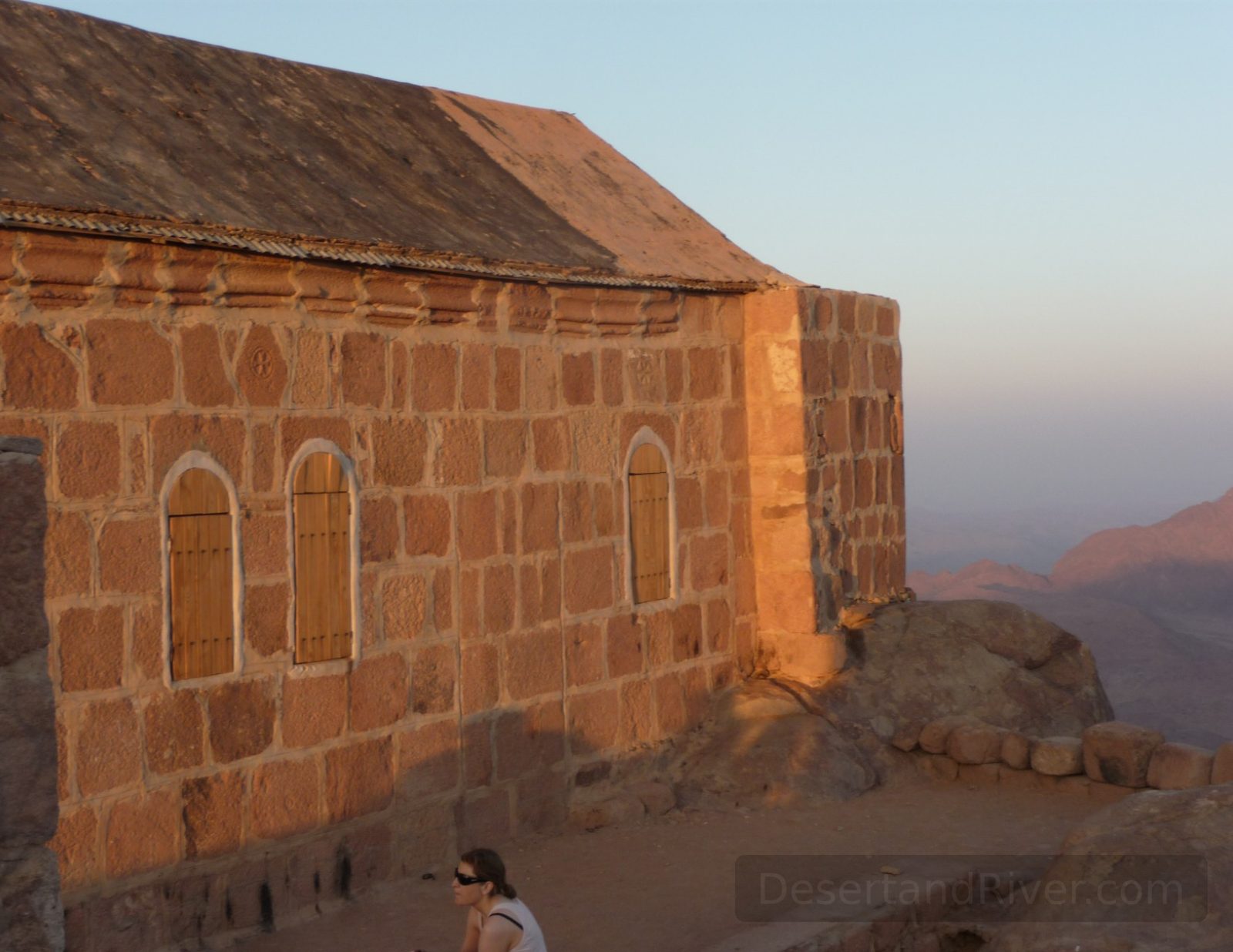 Stone building on Mount Sinai at sunrise, overlooking hazy mountain ridges in the southern Sinai Peninsula.