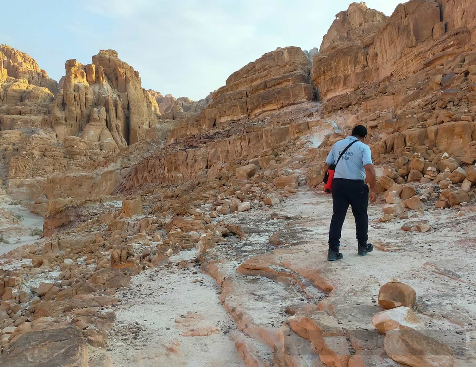 Rocky trail through Nagb el Hemedat mountain pass in Sinai, with a hiker walking across pale sandstone and rugged cliffs.