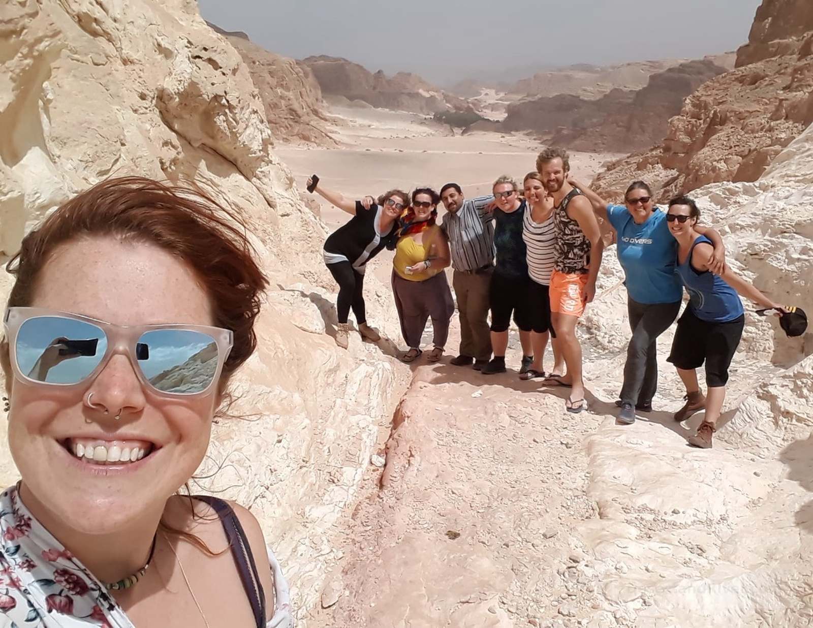 Group of hikers on pale sandstone in Nagb Khudra, southern Sinai, with sun-bleached rock formations and desert hills behind.