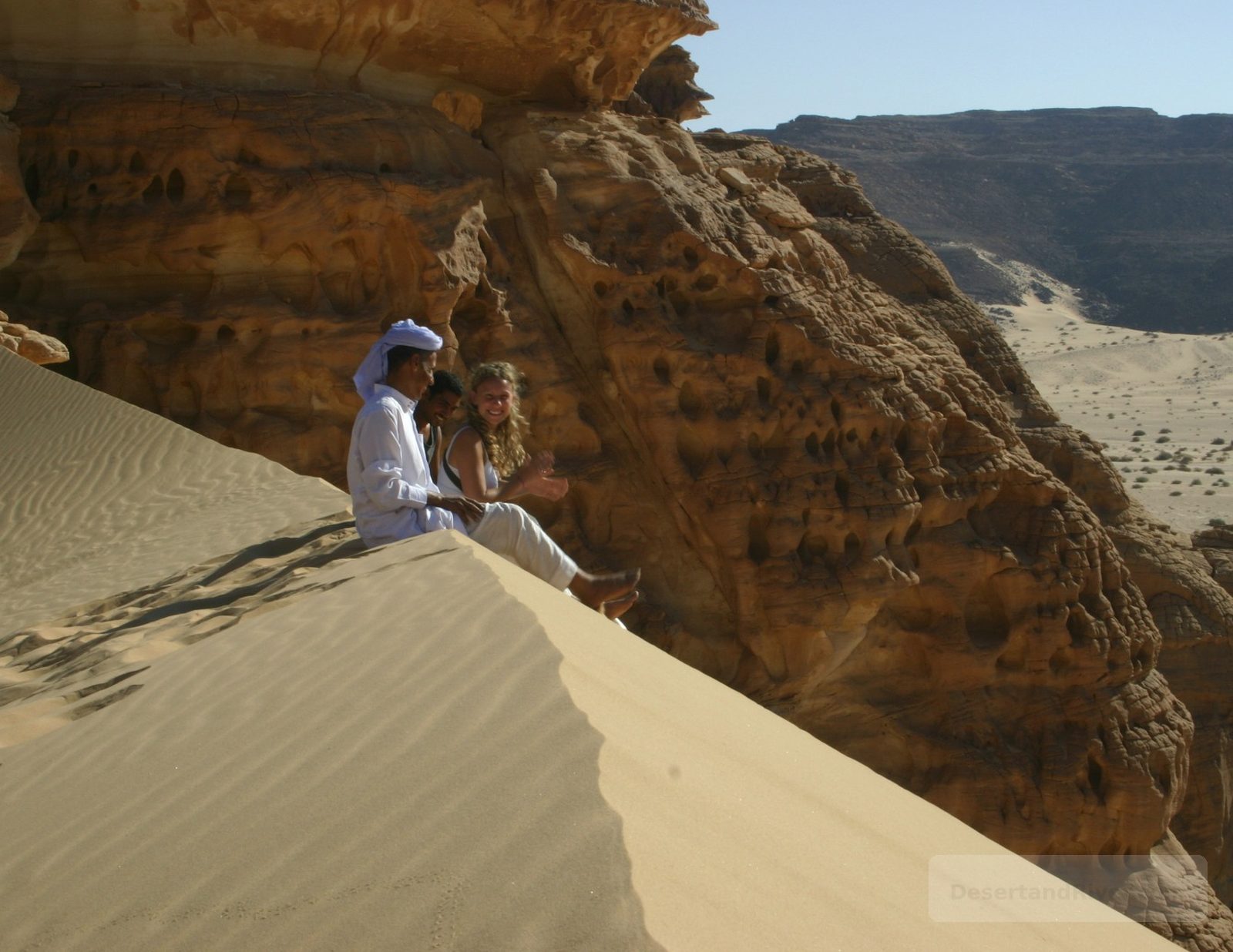 Safra Sand Dune in southern Sinai with golden sand ridges beside weathered sandstone cliffs, overlooking a wide desert plain.