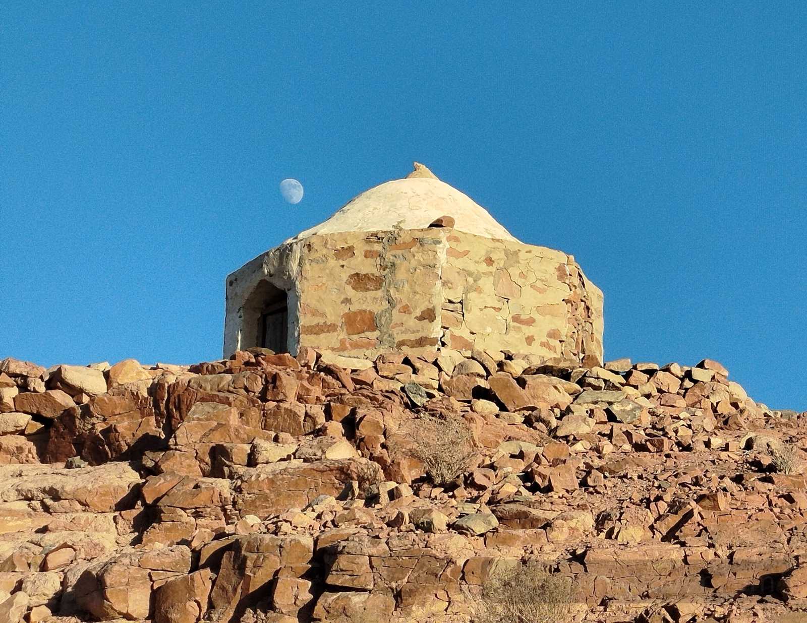 Stone tomb of Sheikh Abu-Taleb on a rocky hill in central Sinai, with the moon visible in a clear blue sky.