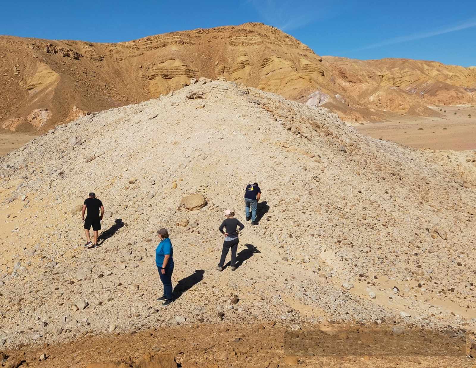 Visitors exploring a pale gravel hill in Wadi Jebi, South Sinai, with layered desert mountains under a clear blue sky.