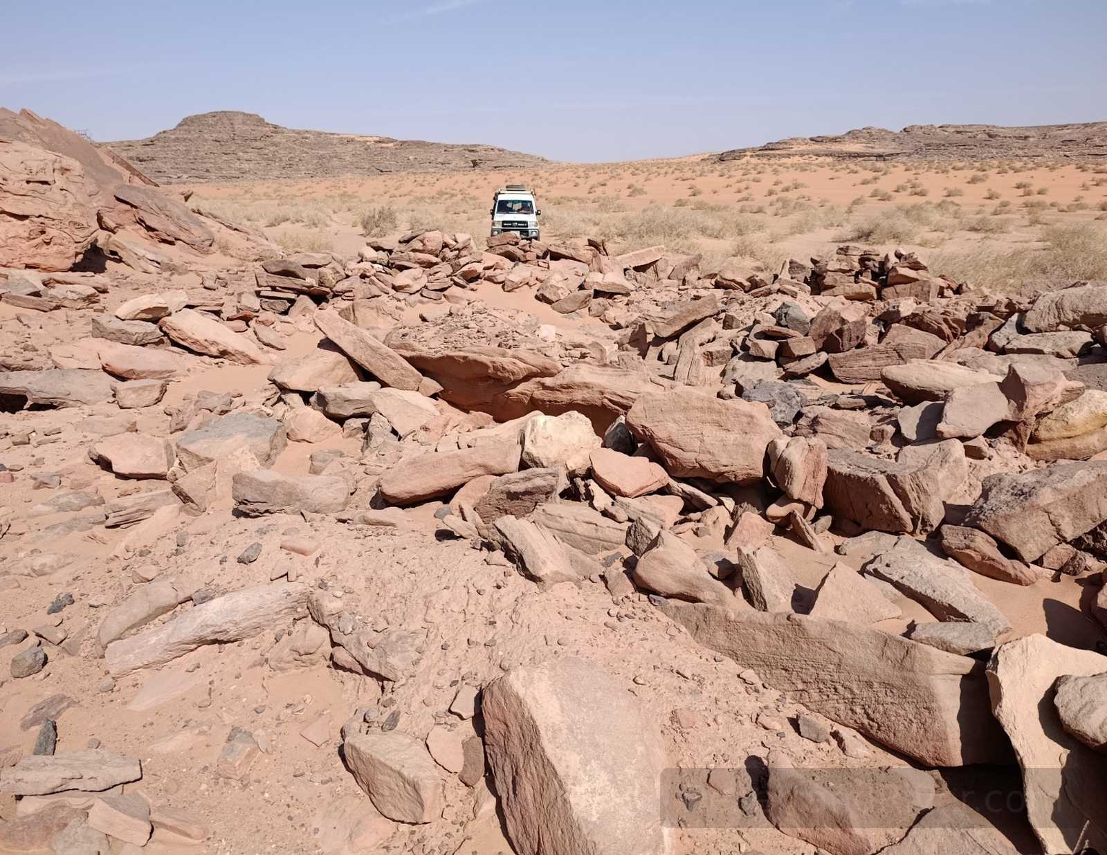 Rocky desert valley in Wadi Khamila, South Sinai, with scattered sandstone blocks and a 4×4 vehicle on a sandy track.
