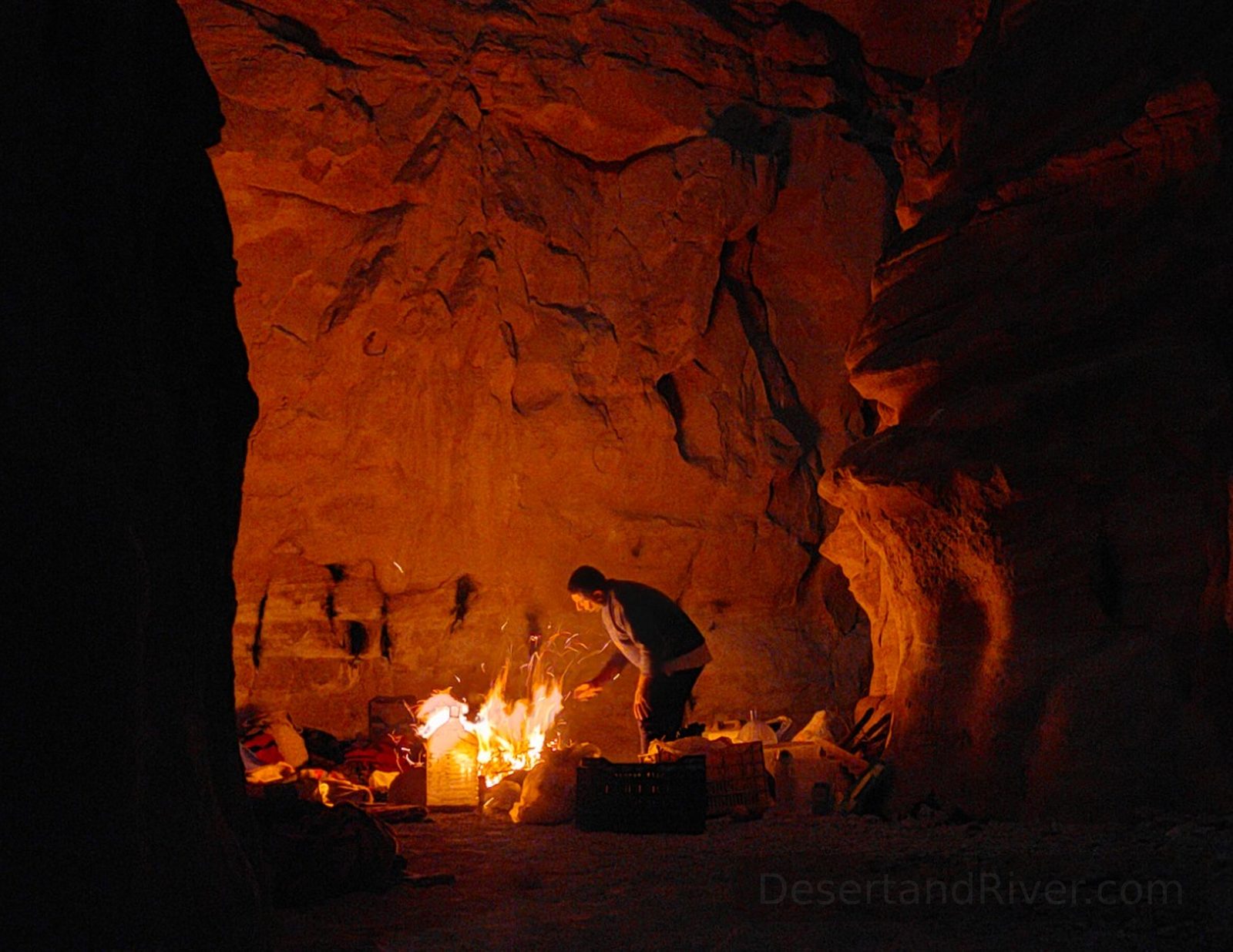 Night camp inside Zig Zag Canyon in southern Sinai, with a small fire illuminating sandstone walls in warm orange light.